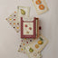 A boxed deck of fruit-themed playing cards labeled 'Watercolour Fruits Playing Cards' by Roomytown, arranged on a light fabric background with several cards fanned out around the box.